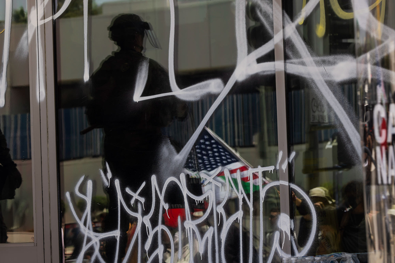 The shadow of a law enforcement officer on a tinted glass wall filled with graffiti.