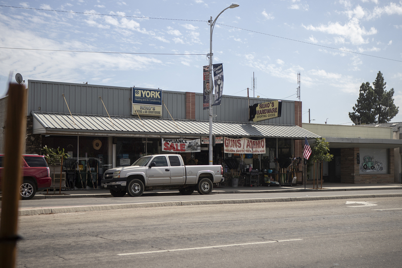 The exterior of a hardware store with trucks parked in front of it on a main road in a small California town.