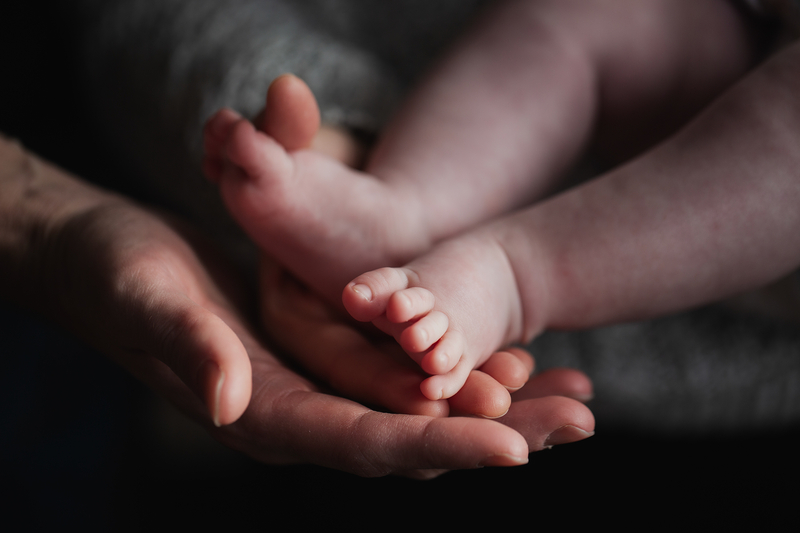 A close-up view of an adult's hand holding the feet of a newborn baby.