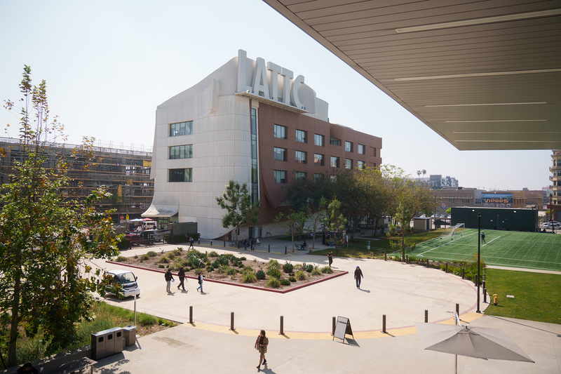 A view of students walking through the campus of a college with a building with the letters "LATTC" written out in big white lettering on the roof.