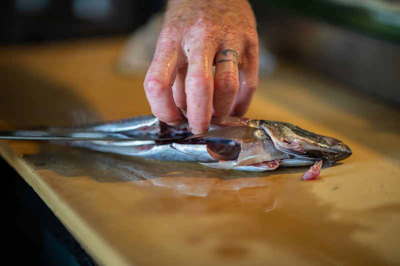 A person's holds open a fish as it is sliced with a knife.
