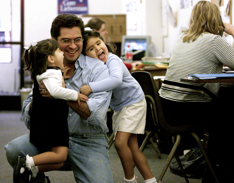 Xavier Becerra smiles as he embraces his two young daughters inside a campaign office.