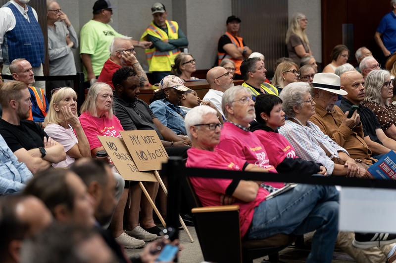 Attendees sit and stand in a crowded room during a Solano County Board of Supervisors meeting, with some holding signs opposing a proposal.