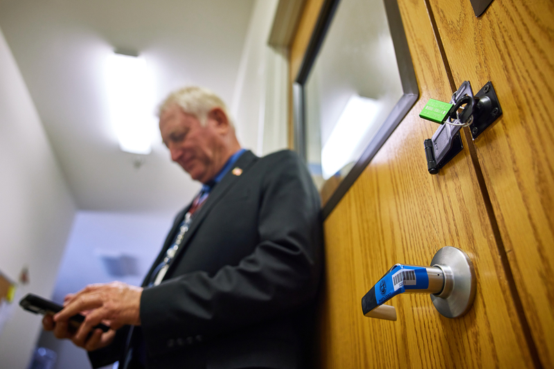 A man in a suit types on his phone next to a wooden door with a green lock and blue seal.