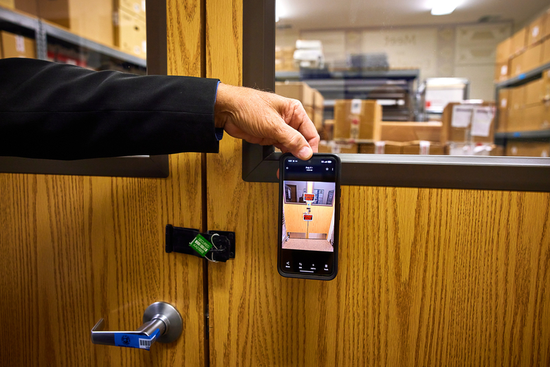 A man uses his phone to show a picture of "Keep Out" signs sealing a door. Next to his phone is the same set of doors with a new green lock and blue seal.