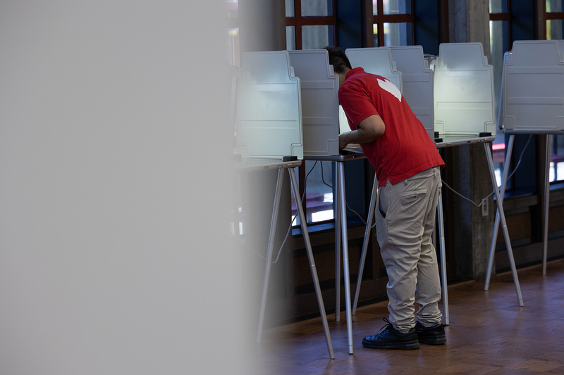 A person in a red shirt stands at a voting booth inside inside of a voting center.