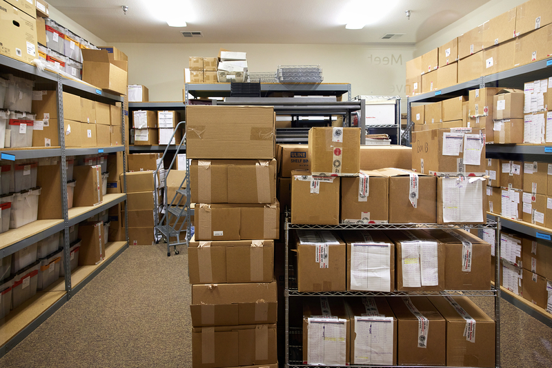 Shelves and carts are filled with sealed and labeled boxes and storage bins inside a secure room.
