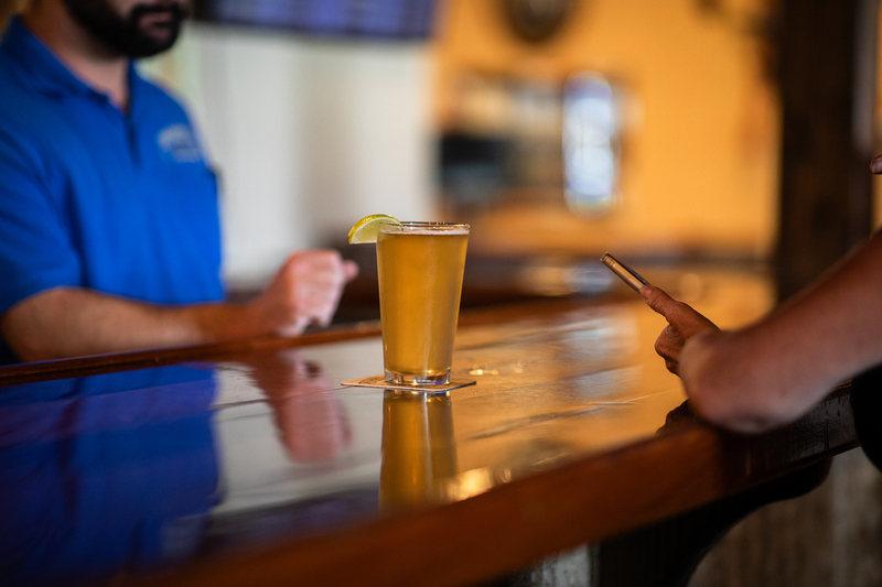 A glass of beer sits on a bar counter in between a bartender and a guest.