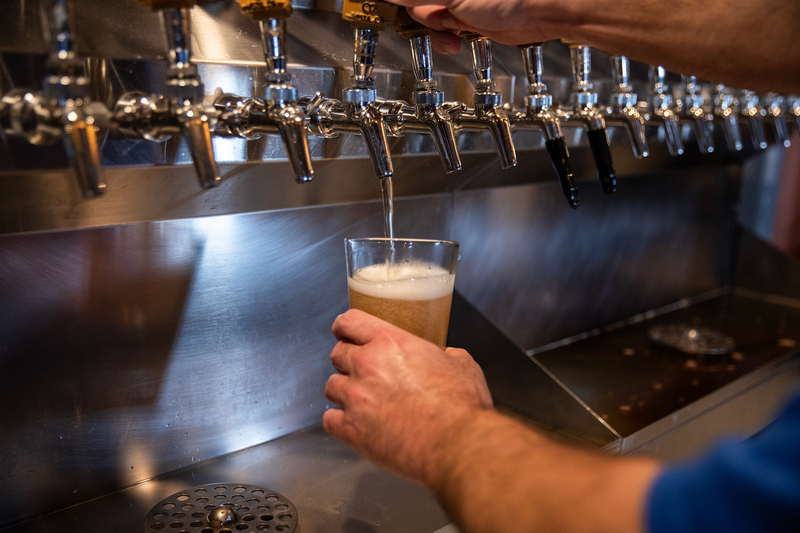 A close-up of a person pulling a handle to pour beer onto a class.