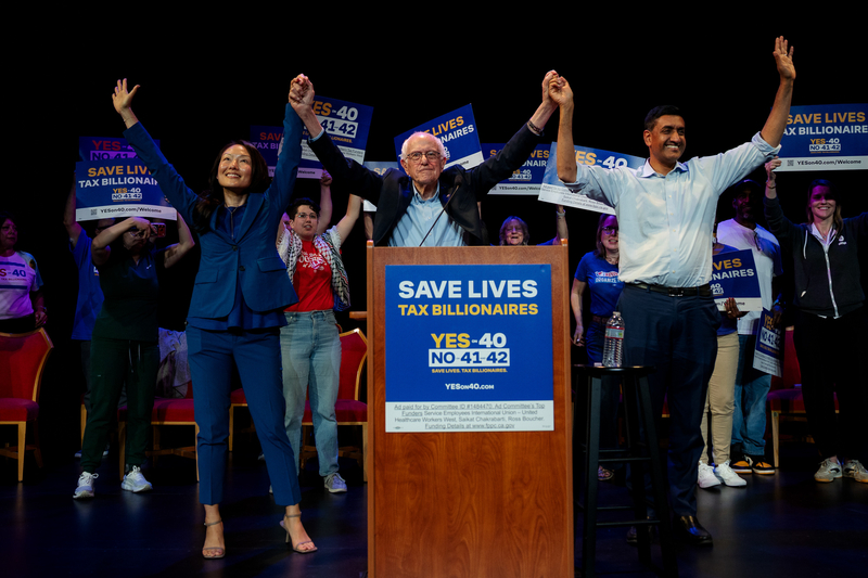 Three politicians hold hands and wave from behind a podium with a Proposition 40 sign on it.