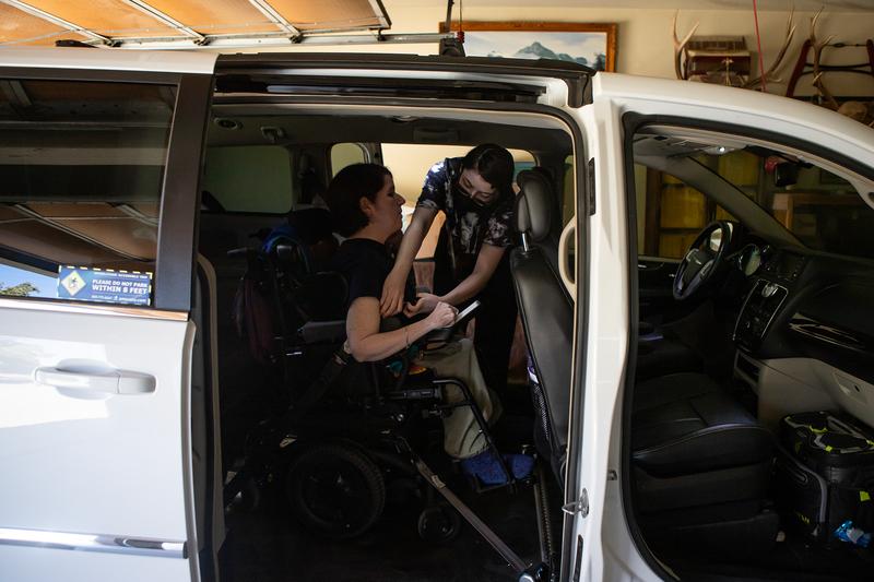 A person helps secure another person in a wheelchair inside a van.