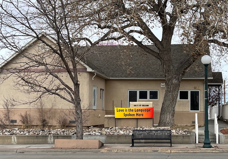 A tan building with a sign out front that says "love is the language spoken here"