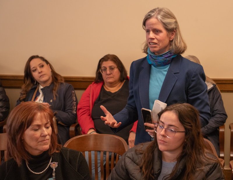 Christine stands by her chair in a committee meeting room at the capitol