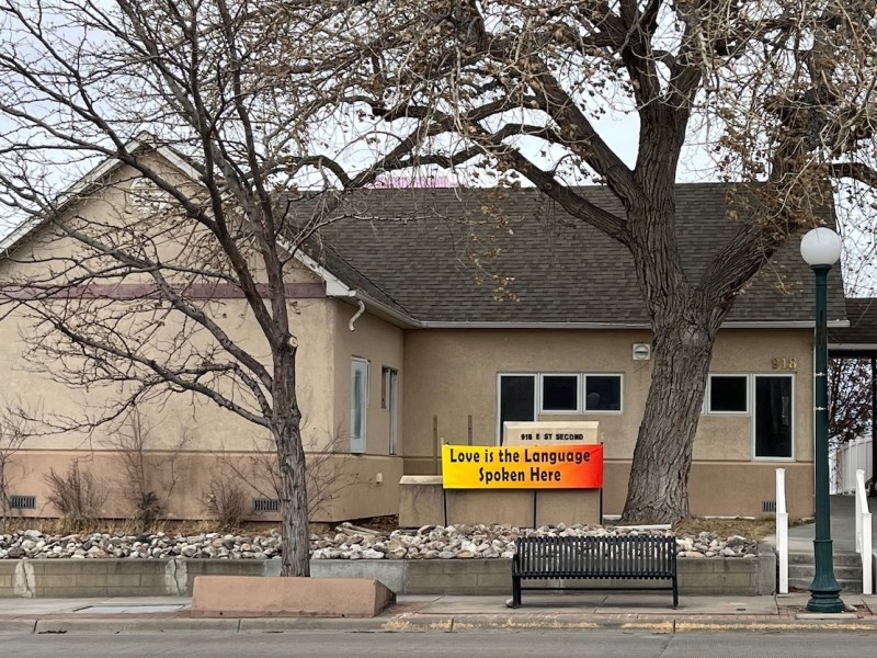 A tan building with a sign out front that says "love is the language spoken here"