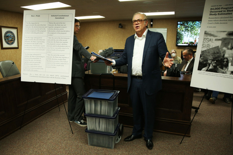 Dakotans for Health Executive Director Rick Weiland, standing beside copies of petition sigantures, speaks to the press about an initiated constitutional amendment to enshrine abortion in the constitution at the South Dakota Capitol in Pierre on Feb. 7, 2024. (Makenzie Huber/South Dakota Searchlight)