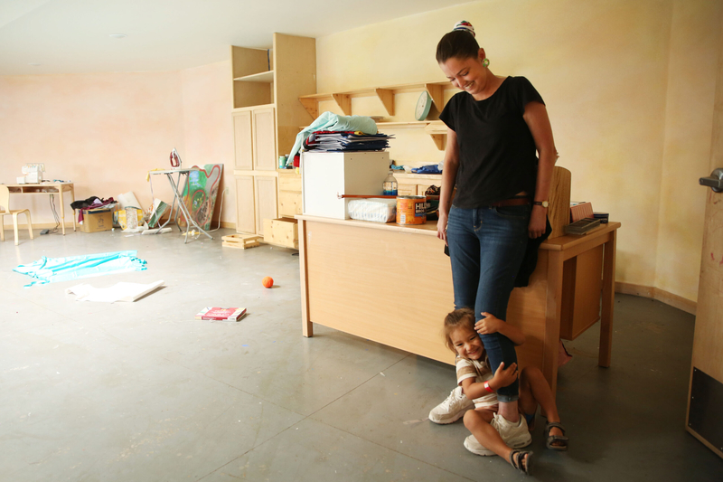 Celestine Stadnick stands in a Lakota Waldorf classroom cleaned out for summer break on July 30, 2024, her nephew hanging onto her leg. Lakota Waldorf is located in Kyle, South Dakota on the Pine Ridge Reservation. (Makenzie Huber/South Dakota Searchlight)