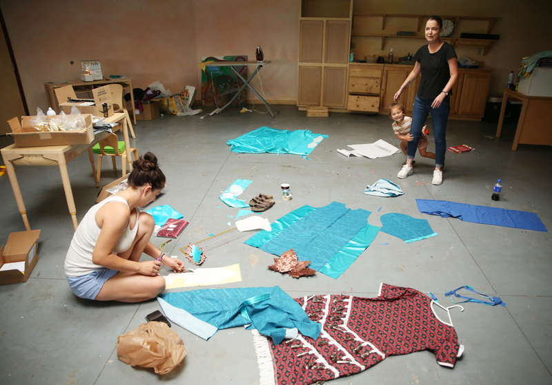 Caroline Stadnick, the 7th and 8th grade teacher at Lakota Waldorf, sews traditional dancing dresses for students on July 30, 2024. Her son plays with his aunt, Celestine Stadnick, while she works. Lakota Waldorf is located in Kyle, South Dakota on the Pine Ridge Reservation. (Makenzie Huber/South Dakota Searchlight)