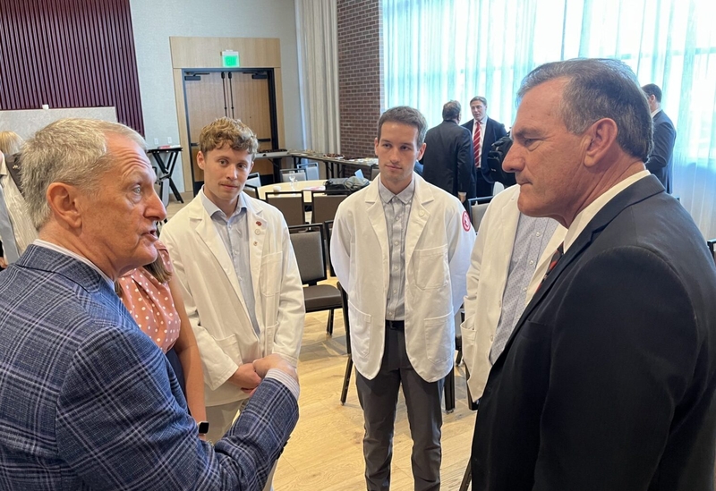 From left, Tim Ridgway, vice president of health affairs and Sanford School of Medicine dean, speaks with medical students including Tanner Smith and Tanner Berg, as well as South Dakota Gov. Larry Rhoden, at the Canopy by Hilton in downtown Sioux Falls on Aug. 14, 2025. (Makenzie Huber/South Dakota Searchlight)