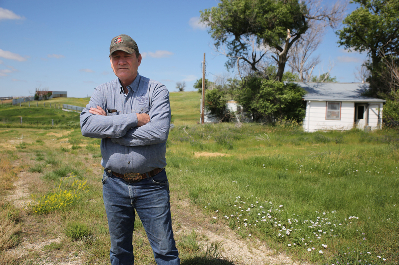 South Dakota Gov. Larry Rhoden stands in front of the small house he was raised in with four siblings and his two parents during a tour of his Union Center ranch on June 26, 2026. The vacant structure stands less than 300 feet from the home he built with First Lady Sandy Rhoden and raised four sons in. (Photo by Makenzie Huber/South Dakota Searchlight)