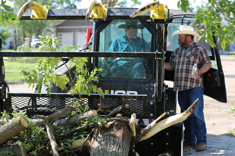 Sal Roseland, right, of Seneca, South Dakota, talks with Gov. Larry Rhoden as Rhoden operates Roseland's skid-steer loader on June 29, 2026. Roseland drove to Highmore after severe storms to assist cleanup efforts. (Photo by Meghan O'Brien/South Dakota Searchlight)