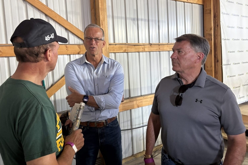 U.S. Senate Majority Leader John Thune and Sen. Mike Rounds, both Republicans from South Dakota, speak with an attendee of Dakotafest in Mitchell on Aug. 19, 2026. (Photo by Joshua Haiar/South Dakota Searchlight)