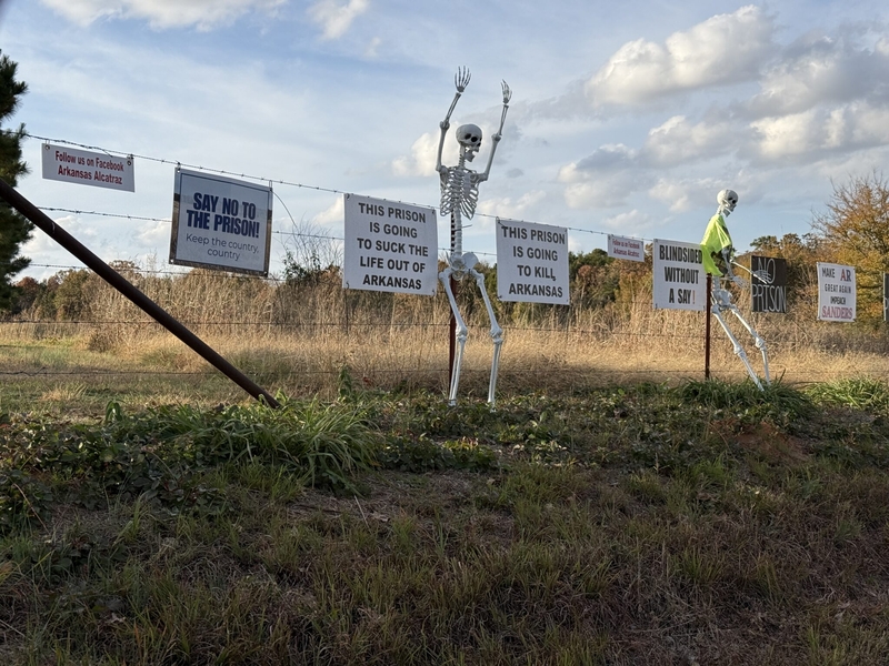 Signs of opposition to the Franklin County prison decorated the fence directly across the street from the prison site's entrance on Arkansas Highway 215 on Nov. 13, 2025. (Photo by Ainsley Platt/Arkansas Advocate)