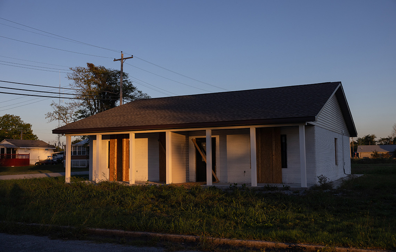 Sunset light illuminates an unfinished house that is partially boarded up.