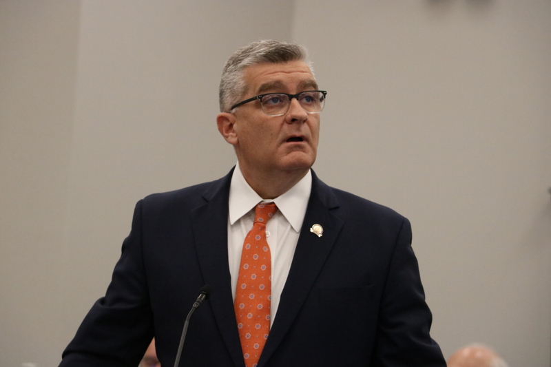 Mills stands in front of a microphone.