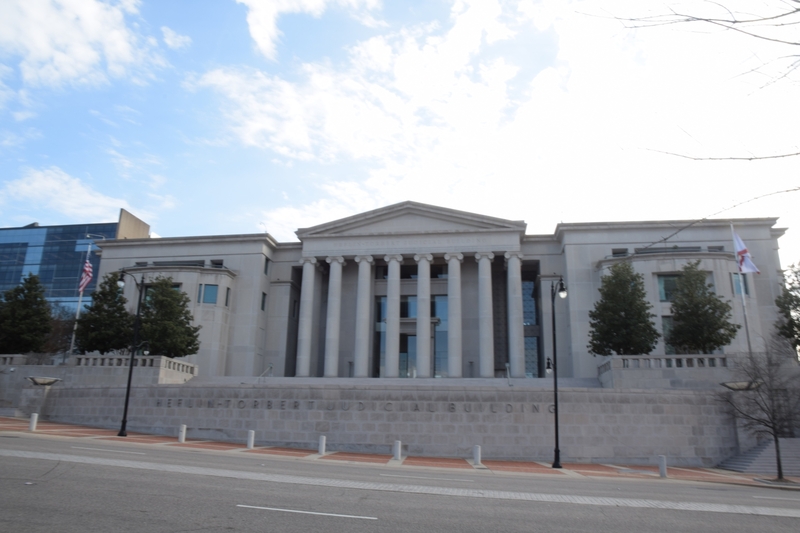 The words "Heflin-Torbert Judicial Building" are seen on a brick base. A classical style facade, with eight columns supporting a triangular tympanum. On each side are square wings, holding offices.