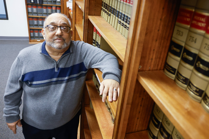 A man resting his arm on a bookshelf with legal texts.