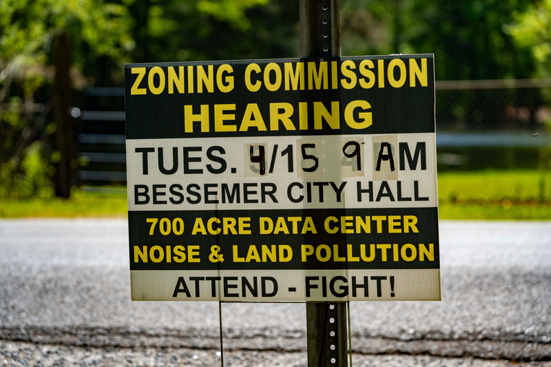 A sign saying "Zoning Commission Hearing Tuesday 4/15 9 a.m. Bessemer City Hall 700 Acre Data Center Noise and Land Pollution Attend - Fight!