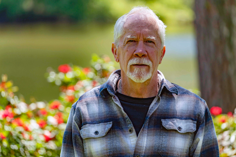 A man in a flannel shirt standing in front of a rose bush