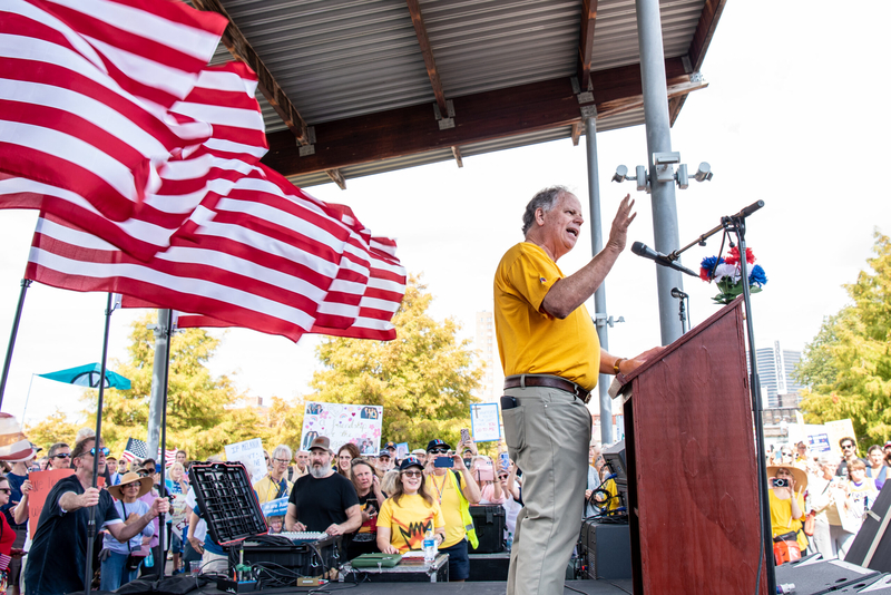 A man in a yellow T-shirt and slack addressing a crowd