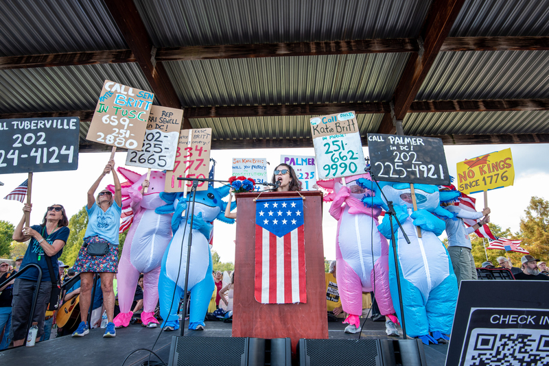 A woman speaking at lectern flanked by people in inflatable suits
