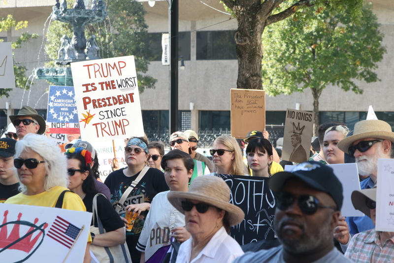 A crowd of people including a person holding a sign saying "Trump is the worst president since Trump"