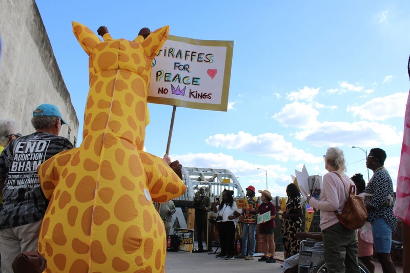 A person in a giraffe suit holding a sign saying giraffes for peace no kings