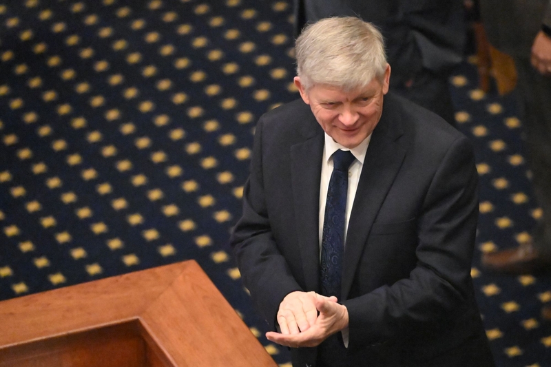 A man in a dark suit with his hands resting in each other