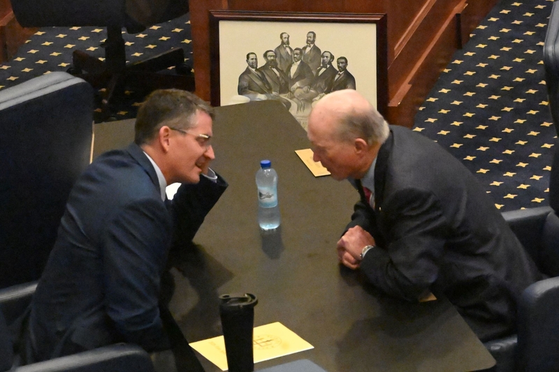 Two men speaking next to a lithograph