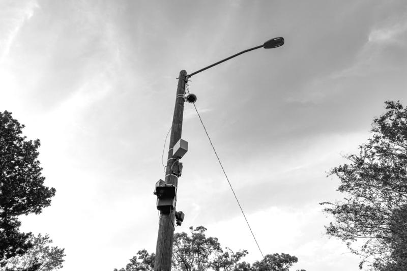 A black and white photo of a pole with wires and surveillance equipment attached