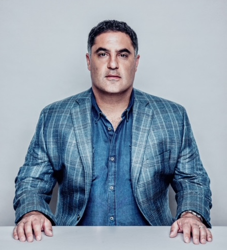 A man in a blue shirt and suit jacket sits at a white table
