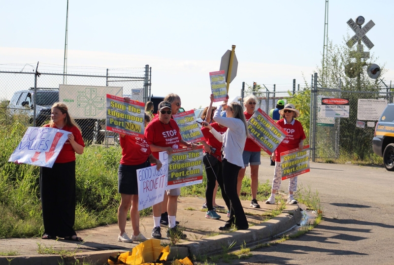 A group of protesters dressed in red shirts hold up signs protesting the Edgemoor port expansion.
