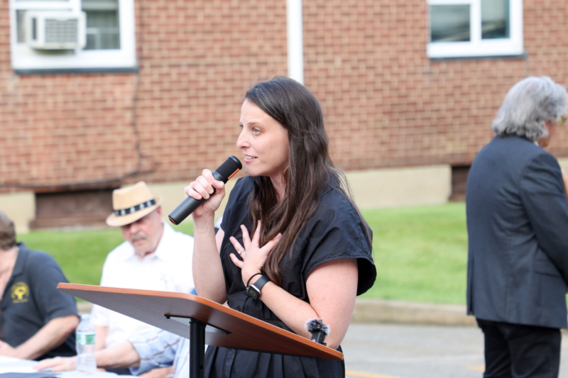 Photo of Jane Menton speaking into a microphone at a podium outdoors.