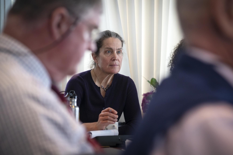 A woman sitting at a table in front of a group of people.