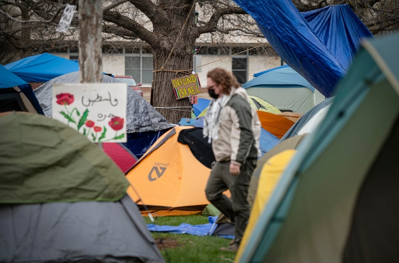 A person walks through a crowded tent encampment with various colorful tents and a sign reading "defund police.