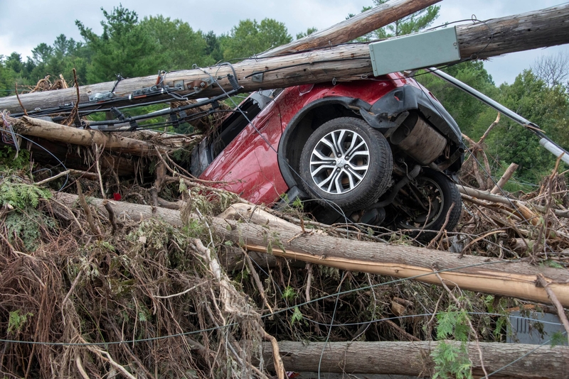 A red SUV is overturned and entangled in fallen trees and debris after a severe storm.