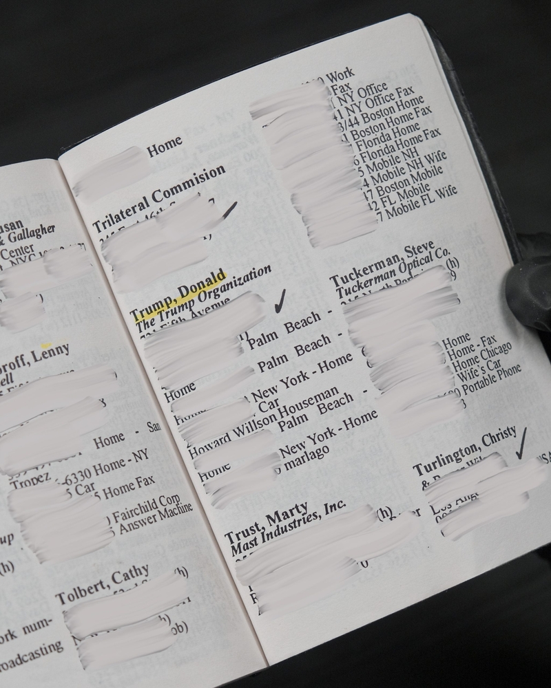 A gloved hand holds an open address book; several entries are redacted, with "Trump, Donald The Trump Organization" visible in the center.