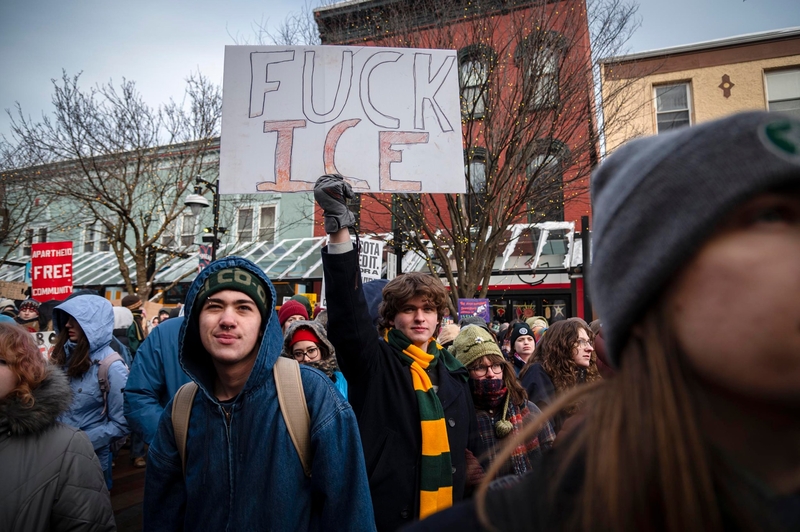 A group of people at a protest; one person in the center holds a sign that reads "FUCK ICE.