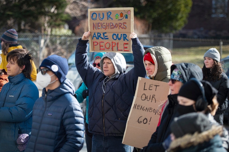 A group of people at an outdoor protest hold signs that read "OUR NEIGHBORS ARE OUR PEOPLE" and "LET OUR NEIGHBORS GO!" while dressed in winter clothing.