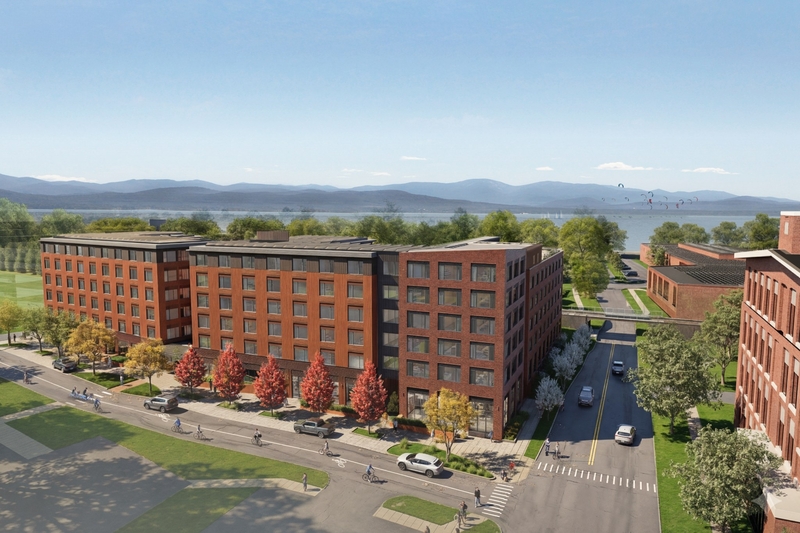 A rendering of a modern brick apartment complex with tree-lined streets, parked cars, and a distant lake with mountains in the background.