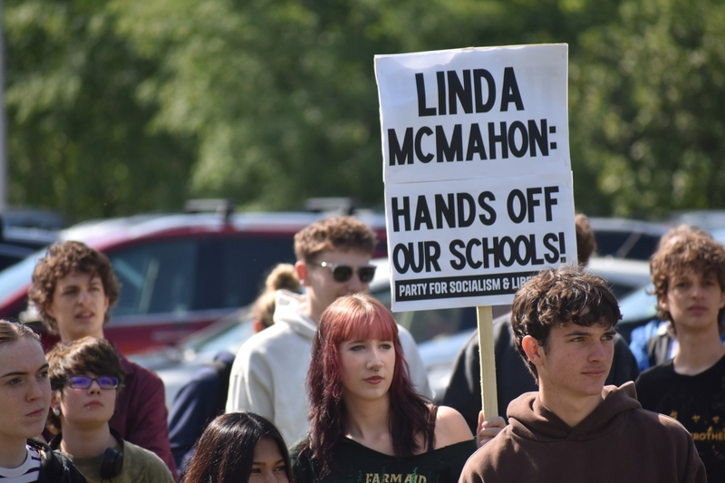 A group of young people at a protest, one holding a sign that reads, “Linda McMahon: Hands off our schools! Party for Socialism &amp; Liberation.”.